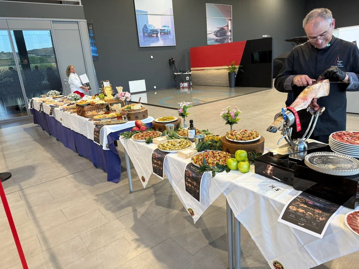 Mesa de buffet con quesos, embutidos y aperitivos junto al cortador de jamón, en un catering de San Remo para la presentación de un vehículo